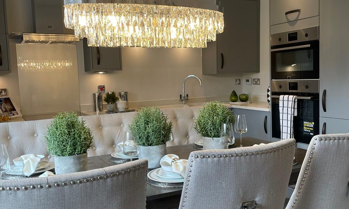 Open plan kitchen diner with grey dining chairs, plant pot centrepieces and a low hanging chandelier